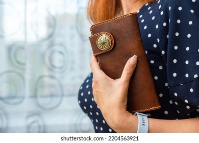 Woman holds a brown natural leather wallet in her hand. Wallet made of genuine leather, a beautiful and practical women's accessory.