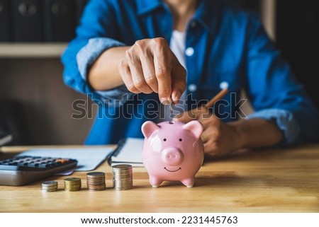 woman holds a coin in a pig-shaped piggy bank to save money for the future. after retirement and record keeping of income, expenditure, savings and financial concepts.