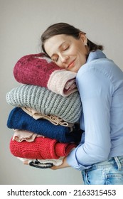  Woman Holds Colored Sweaters And Clothes In Her Hands. Washing And Care Of Clothes, Powder And Conditioner For Washing. Happy Woman Stylist Picks Up Clothes, Recycling Clothes And Charity Donation