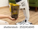 Woman holds a container for collecting dust from vacuum cleaner. Vacuum cleaner garbage collection container