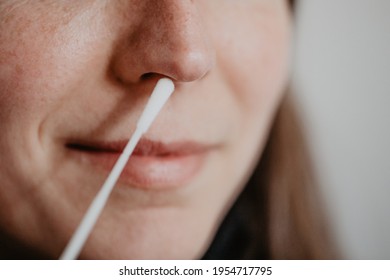 Woman holds corona test smear to nose to test herself for COVID-19 with antigen test