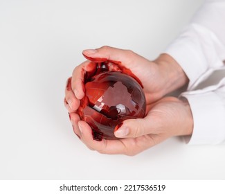 A Woman Holds A Crystal Globe Smeared In Blood On A White Background.