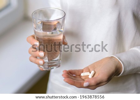 A woman holds a glass of water and two pills in her hands. Young woman treats illness with pills. Headache or stomach problems and treatment with medication. Antibiotic treatment concept