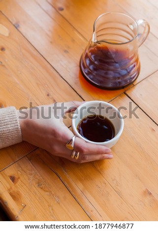woman holds in hand a ceramic mug with black coffee. alternative brewing of specialty coffee. background light wood