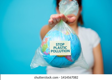 Woman holds in hands plastic bag with sticker text stop plastic pollution and planet earth at blue background. The concept of plastic pollution.