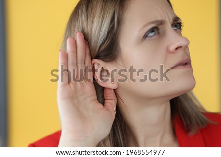 Woman holds her hand near her ear to hear better