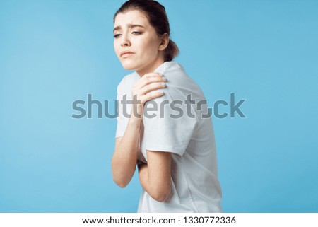 A woman holds her hand over her shoulder on a blue background