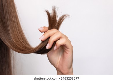 A woman holds in her hand a strand of hair with damaged, dry, split ends, close-up. Isolated on a white background. Hair care concept. Beauty and health. Treatment. Hairdressing services. A haircut