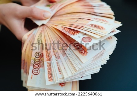 a woman holds in her hands a fan of banknotes of 5000 rubles on a black background. the concept of depreciation of the ruble. earnings online in Russia.