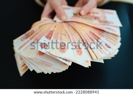 a woman holds in her hands a fan of banknotes of 5000 rubles on a black background. the concept of depreciation of the ruble. earnings online in Russia.