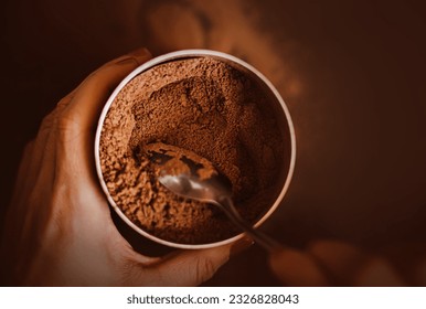A woman holds in her hands a jar filled with fragrant natural cocoa powder, which she takes out with a teaspoon. The process of making a delicious invigorating pleasant drink for breakfast.