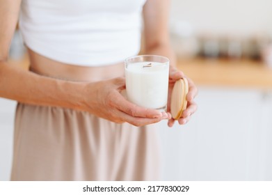 Woman Holds In Her Hands White Candle With Wooden Lid. Blurred Background. Scented Candle Handmade For Comfort At Home.