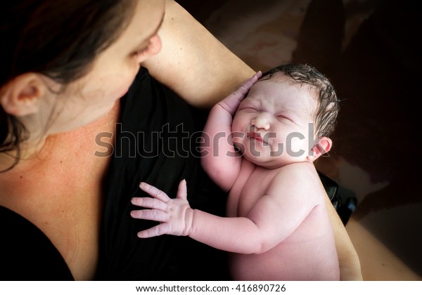 A woman\
holds her newborn son right after giving birth, they are still in\
the birthing pool after labor at\
home.