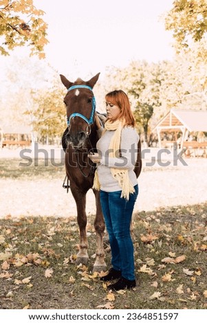 A woman holds a horse by the reins. Horseback riding in the autumn forest. Horse rental. High quality photo