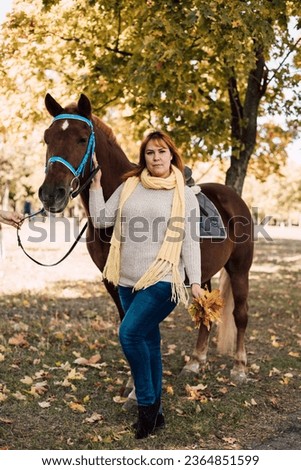 A woman holds a horse by the reins. Horseback riding in the autumn forest. Horse rental. High quality photo