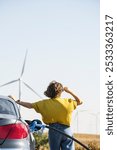 Woman holds a hydrogen fueling nozzle. Refueling car with hydrogen fuel. Wind turbines in the background.