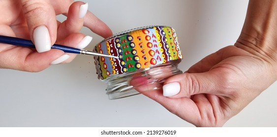 A woman holds a jar in her hands. Spot painting on glass, workshop. Drawing lesson for children in peacetime. Decorates the jar. Multicolored stained glass paints.Ideas for the decoration of objects. 