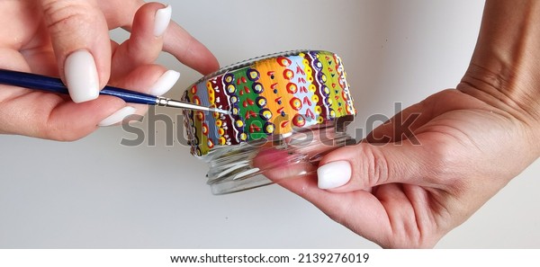 A woman holds a jar in her hands. Spot painting\
on glass, workshop. Drawing lesson for children in peacetime.\
Decorates the jar. Multicolored stained glass paints.Ideas for the\
decoration of objects. 