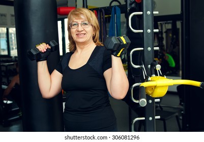 Woman Holds Up Lifting Dumbbells. Client Fitness Center. Woman - Fitness Gym. Senior Exercising At Gym. Old Woman Exercising With Weights At Gym.