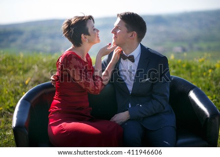 Woman holds man's chin while sitting on the black couch in the field