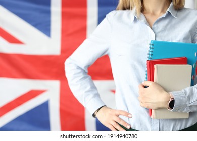 Woman Holds Notebooks And Diaries Against Background Of Flags Of Britain. Language Courses And Training Concept