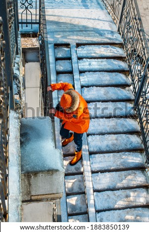 Woman holds onto the railing and goes down the slippery stairs. Uncleaned stairs after heavy snowfall. Frosty snowy weather. Winter in the city.