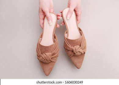 Woman Holds A Pair Of Beige Mule Shoes.