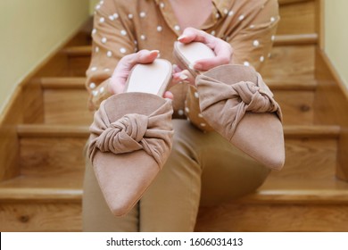 Woman Holds A Pair Of Beige Mule Shoes.