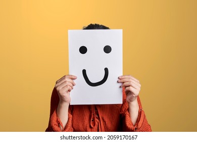 Woman Holds A Paper With Drawn Fake Smile. Woman Hiding Her Feelings And Expressions, Covering Face With Paper And Fake Good Mood Smile