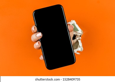 A woman holds a phone through ragged orange drywall