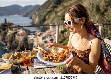 Woman holds plate with seafood at the coast with beautiful landscape of Vernazza village in Italy. Mediterranean food concept. Idea of traveling famous Cinque Terre region