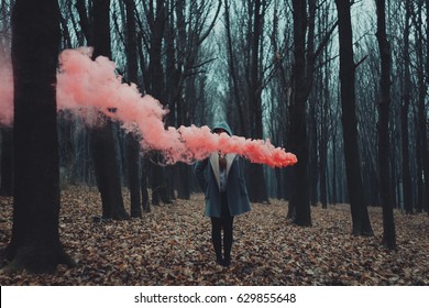 Woman Holds Up Red Smoke Flare To Signal For Help In The Middle Of Nature. Rainy Forest In Mist.