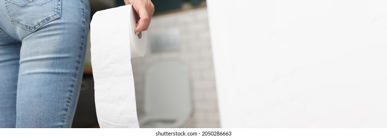 Woman holds roll of toilet paper in her hand while going to toilet