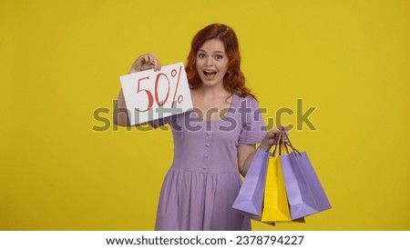 A woman holds shopping bags and shows the inscription fifty percent. Satisfied shopaholic woman in studio on yellow background.