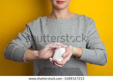 woman holds and shows soap in her hands. Palms and fingers in soapy foam stretch the soap forward, on a yellow background. Hand disinfection in the fight against coronavirus