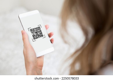 woman holds a smartphone with a qr code and looking on the screen on a white room background