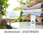 Woman holds a stack of neutral colored knitwear. Recyclable product concept. Organic cotton recycling fabric. Label with recycling icon. Environmental care, reusable, renewable for sustainable living.