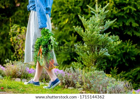 Woman holds a String bag with vegetables in garden