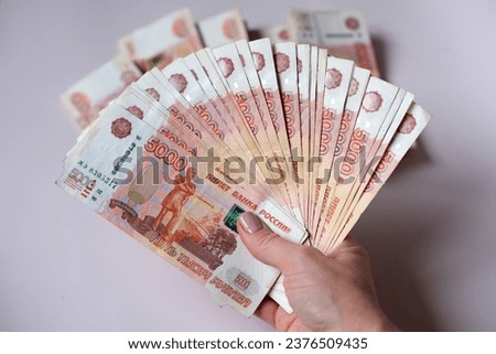 A woman holds a wad of money in her right hand on the background of other money. Million Russian rubles in paper money in a woman's hand. Cash savings in Russia.