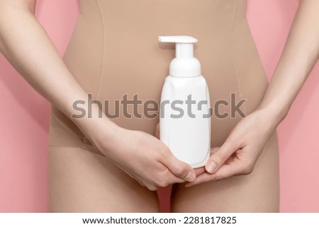 Woman Holds White Bottle Of Hygiene Product, Washing, Cleansing Intimate Gel, Foam. Female Wears Beige Body On Pink Background. Mockup Branding Dispenser, Daily Body Care. Horizontal Plane, Closeup