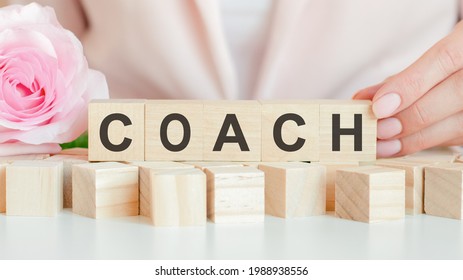 woman holds a wooden cube with the text of coach in her hand. on the wooden cubes there is a living rose flower. pink background, front view. business, economic, education concept