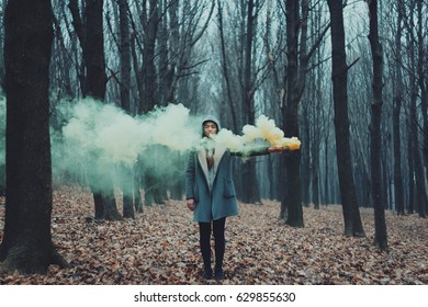 Woman holds up yellow and green smoke flare to signal for help in the middle of nature. Rainy forest in mist. - Powered by Shutterstock