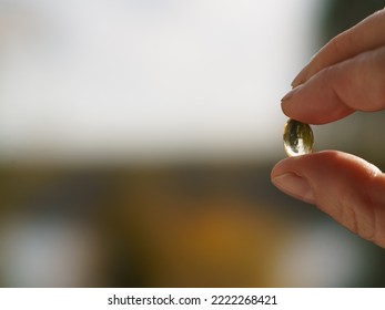 Woman holds the yellow transparent capsule. Vitamin D. The topic of treatment. Close up bright photography in sunny autumn day. Free space for your message. Concept of cure
