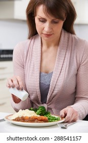 Woman At Home Adding Salt To Meal