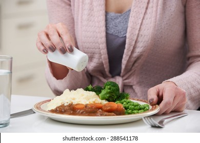 Woman At Home Adding Salt To Meal