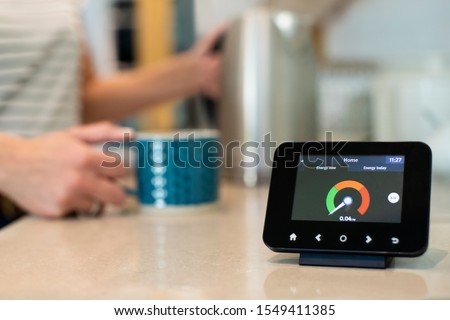 Woman At Home Boiling Kettle For Hot Drink With Smart Energy Meter In Foreground
