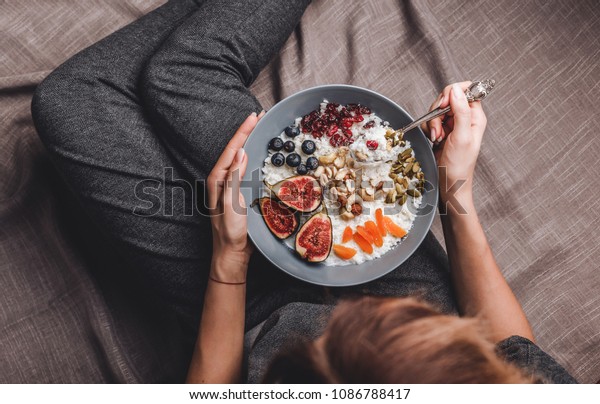 Woman in home clothes eating vegan Rice\
coconut porridge with figs, berries, nuts. Healthy breakfast\
ingredients. Clean eating, vegan food\
concept