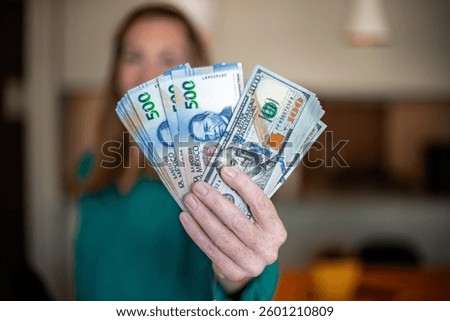 Woman at home displays bundles of 500 Mexican peso and 100 dollar bills