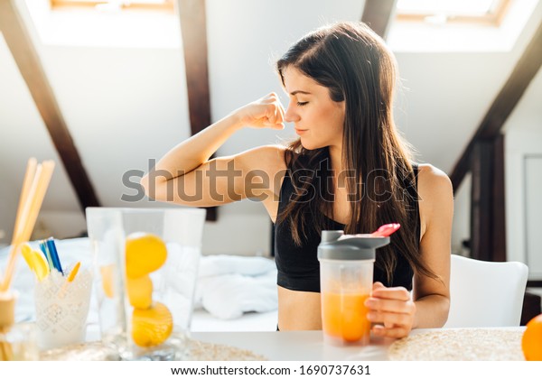 Woman at home drinking orange flavored amino acid\
vitamin powder.Keto supplement.After exercise liquid meal.Weight\
loss fitness nutrition diet.Immune system support.Organic citrus\
fruit drink