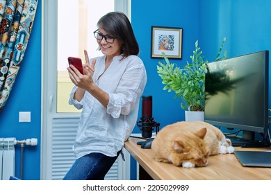 Woman In Home Office Using Smart Phone For Video Call, Cat Sleeping On Desk